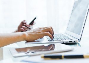 Man inputing data on laptop and holding mobile phone in another hand.